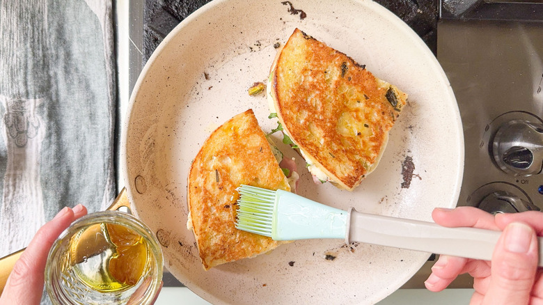 Hand brushing garlic oil on grilled Italian picnic sandwiches in skillet