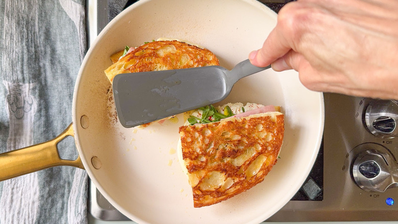 Grilling Italian picnic sandwiches in skillet and pressing down with spatula