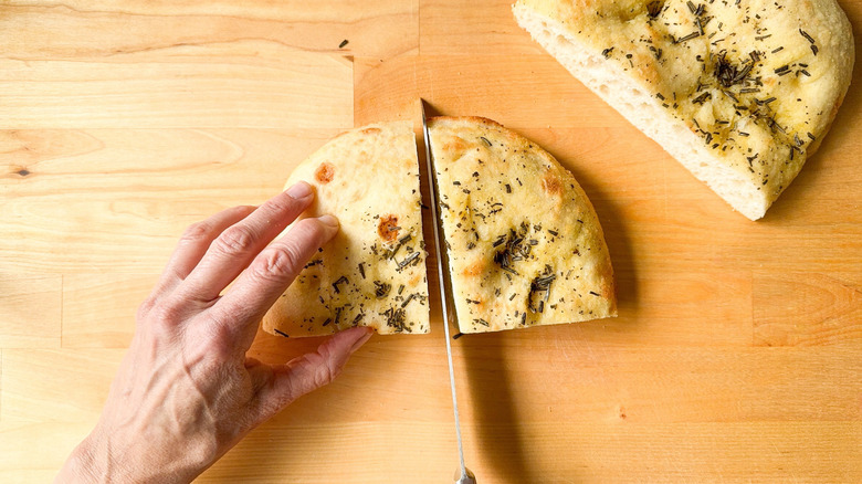 Hand cutting focaccia into even pieces on cutting board