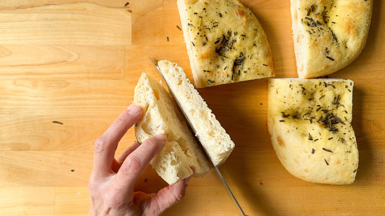 Hand cutting focaccia bread with knife on cutting board