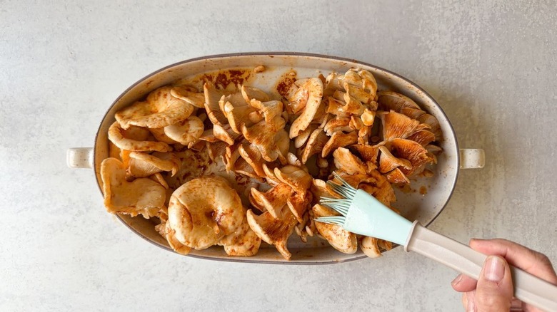 Brushing marinade on oyster mushroom clusters in an oval baking dish