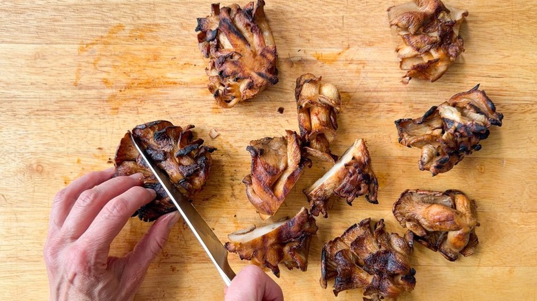 Cutting grilled oyster mushroom clusters on cutting board