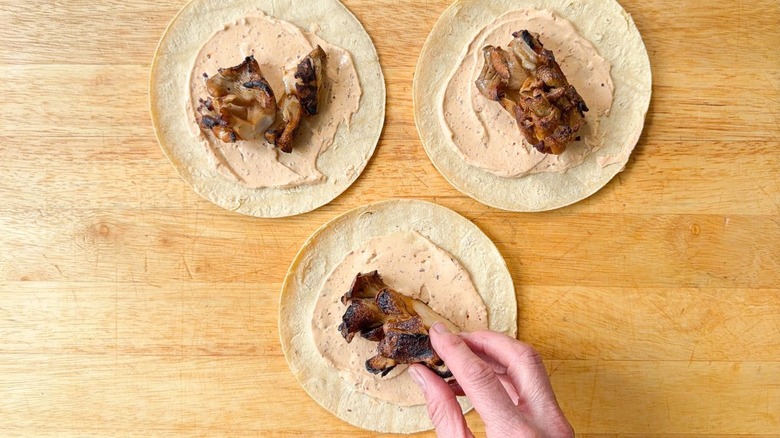 Adding grilled oyster mushrooms to corn tortillas with salsa macha