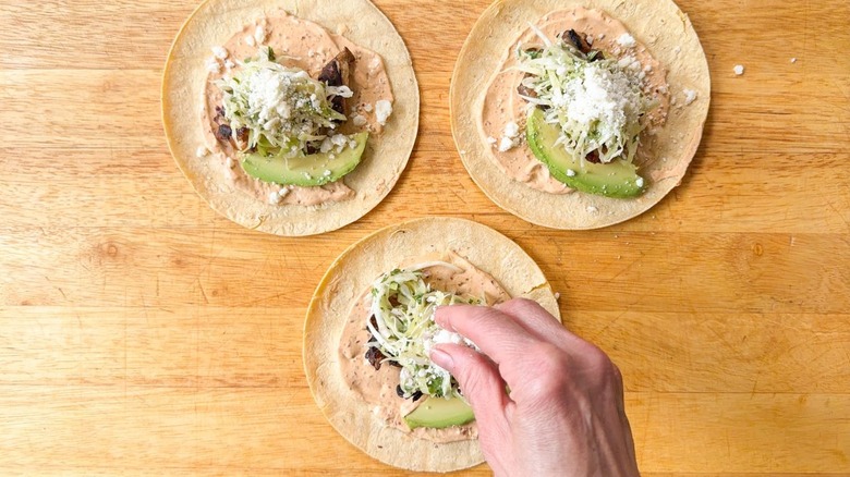 Adding avocado and crumbled cotija cheese to grilled oyster mushroom tacos