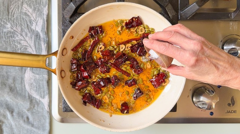 Adding salt to salsa macha ingredients in skillet on stovetop