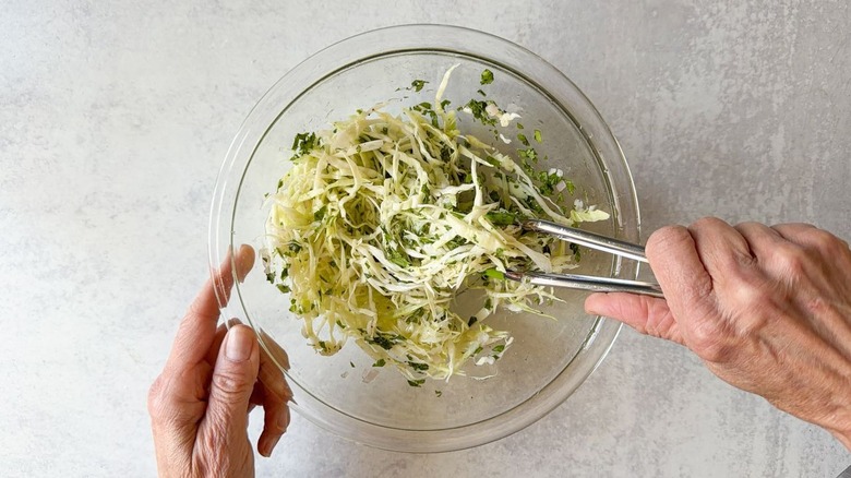 Tossing slaw with tongs in a glass bowl