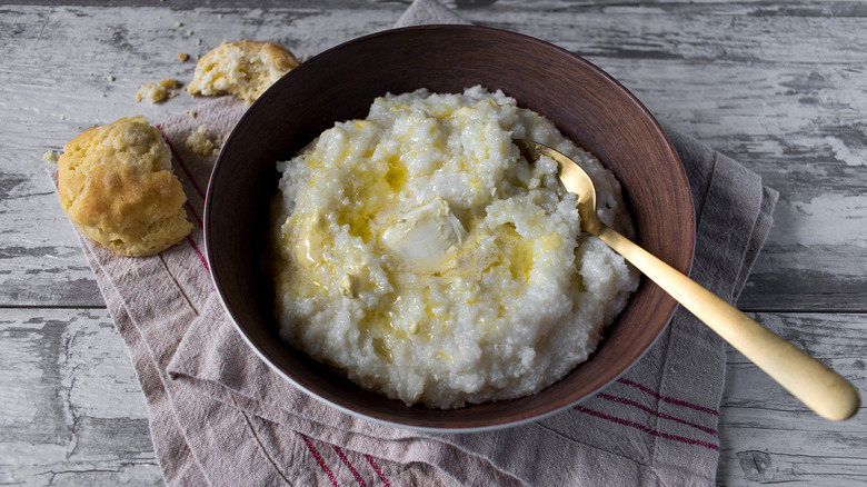 A bowl of grits with a biscuit next to it, torn in two.