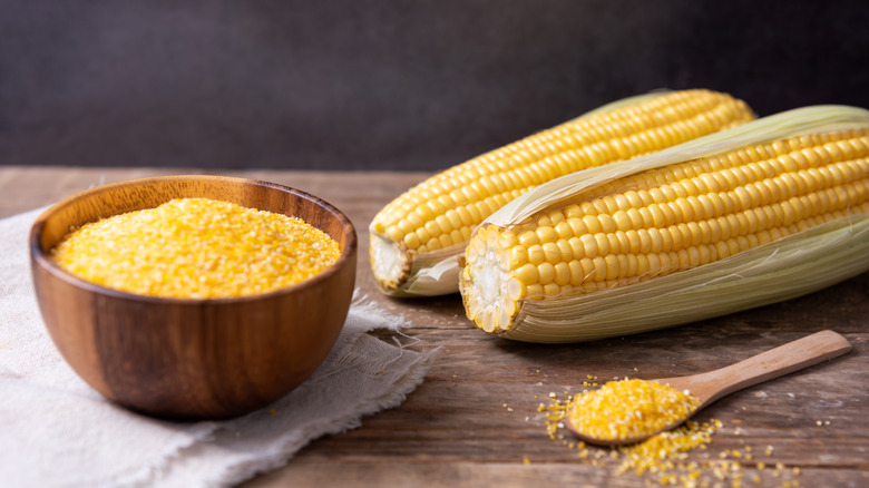 Brown bowl of corn grits next to two ears of corn