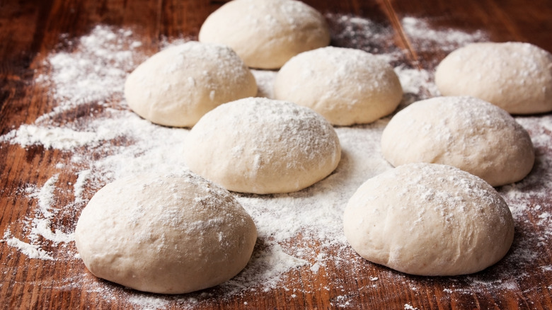 Balls of freshly made pizza dough topped with floor on a wooden table