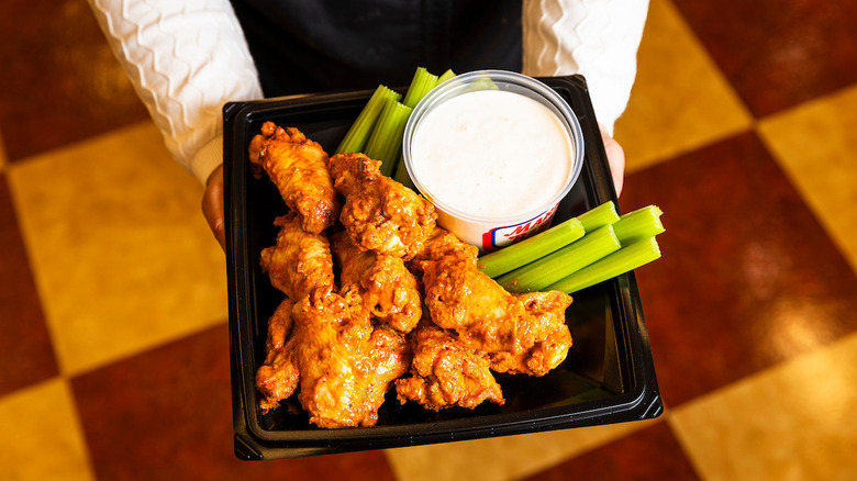 A person holding a tray of chicken wings with celery sticks and dip at Market Basket