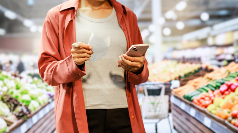Person holding a receipt and smartphone at a grocery store.