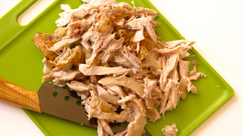A stack of rotisserie chicken meat on a cutting board.