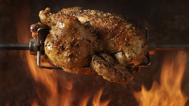 A rotisserie turkey on the spit with flames behind it.