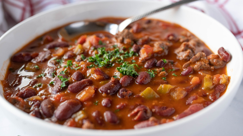 Beans and beef in a red sauce in a white bowl with spoon.