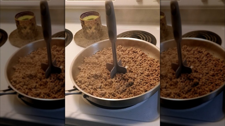 Meat chopper standing up in a pan of ground beef on an electric stove