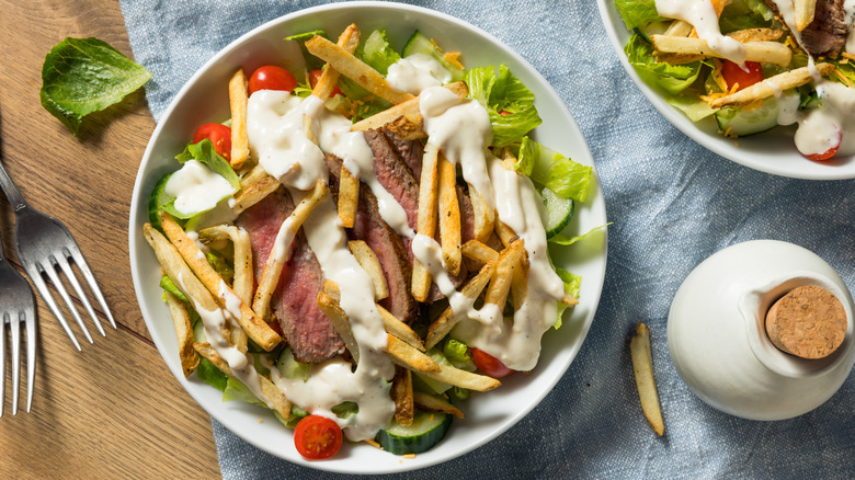 A Pittsburgh style steak salad with fries and meat on top of a salad bed.
