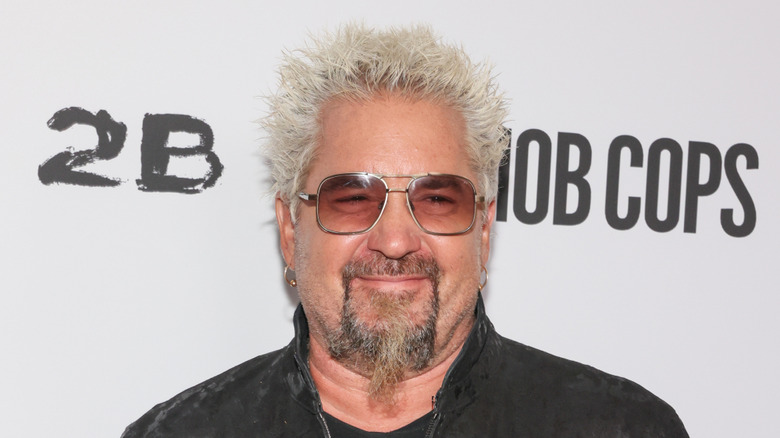 Guy Fieri smiling and wearing sunglasses at a movie screening