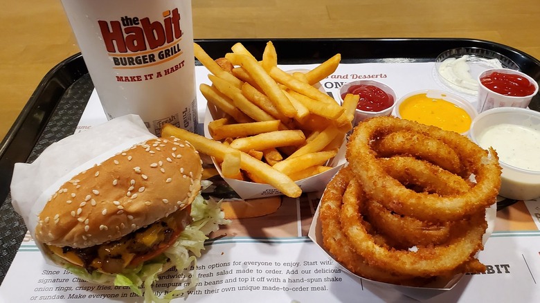A Habit Burger tray with a burger, fries, onion rings, sauces, and a drink