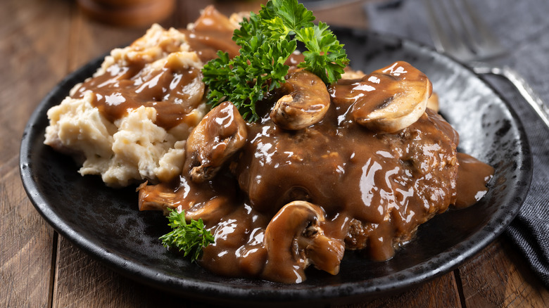 Salisbury steak with a side of mashed potatoes topped with mushroom gravy and parsley