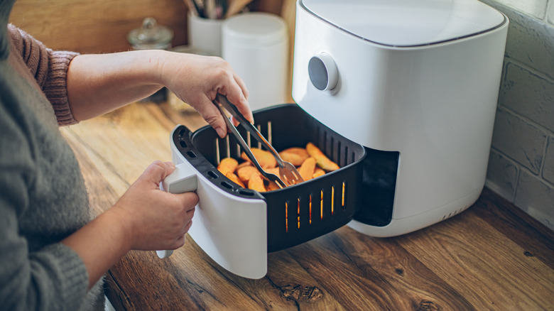 Person using tongs to remove food from an air fryer.