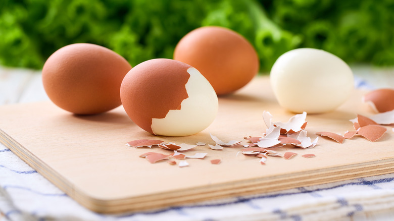Hard-boiled eggs, some with shells removed, on a cutting board outdoors