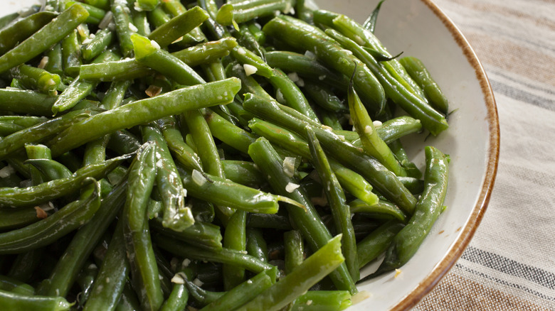 A bowl of cooked green beans with bits of garlic mixed in.
