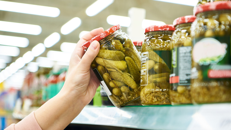 a caucasian hand reaching for a jar of pickles in grocery store