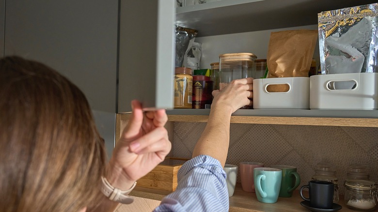 Person grabbing a glass jar off cabinet shelf in kitchen