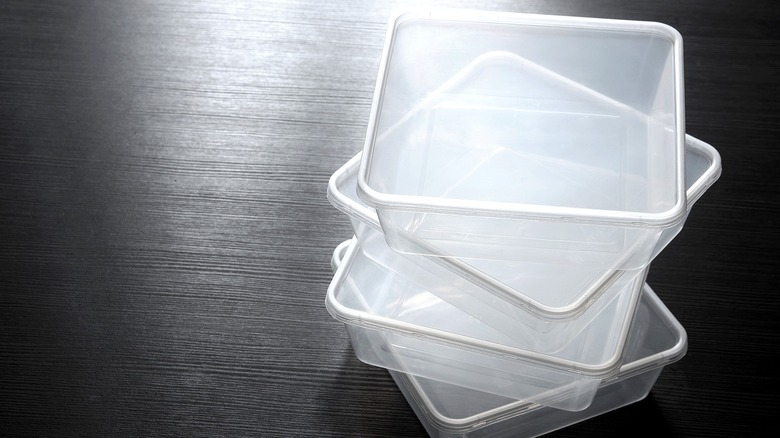 Stack of plastic, square, empty food storage containers on a dark wooden surface