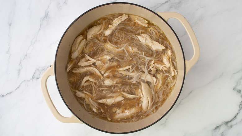 shredded chicken and noodles in a pot of brown liquid