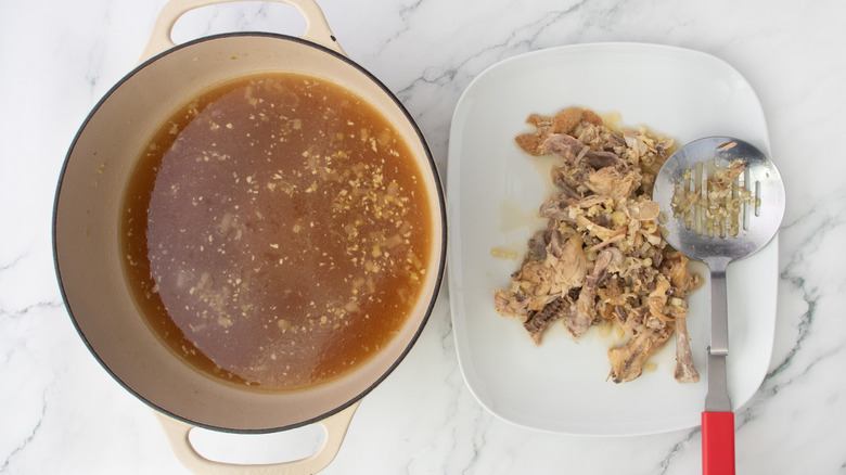 chicken bones on a white plate next to a pot of brown liquid