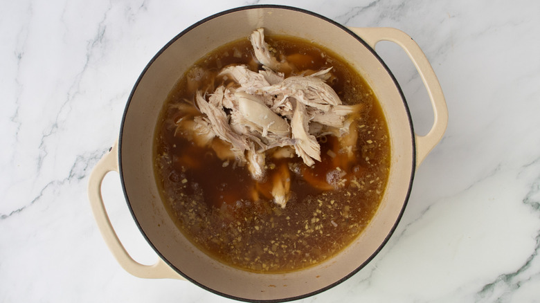 shredded chicken in a pot of brown liquid
