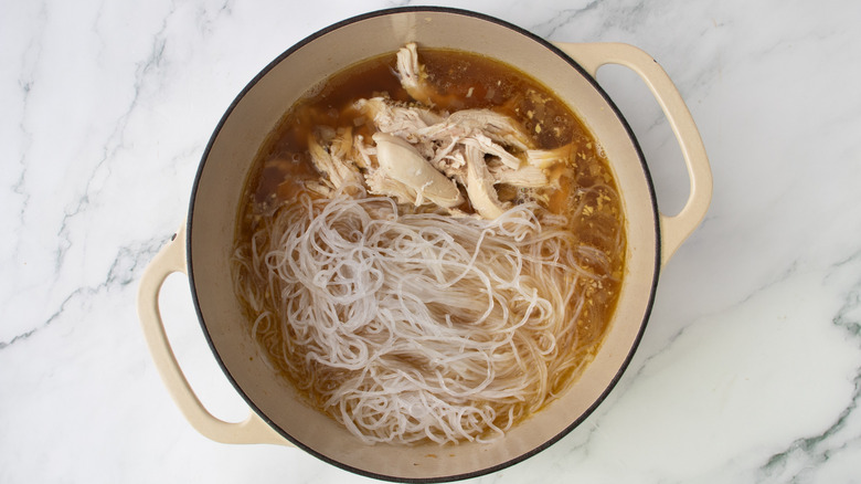 shredded chicken and noodles in a pot of brown liquid