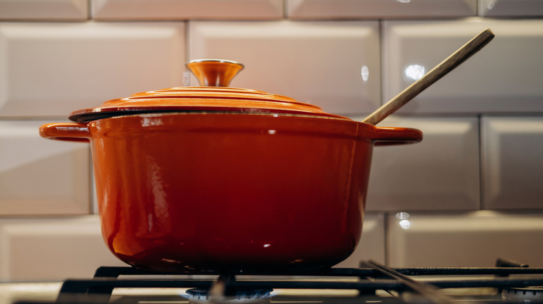 Cast iron Dutch oven on a stovetop with a wooden spoon sticking out of the top