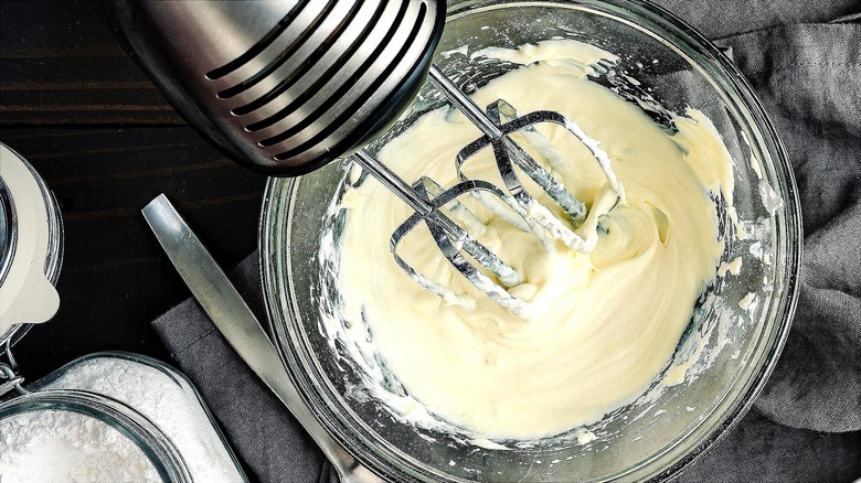 Hand mixer whipping up cream in a large clear bowl