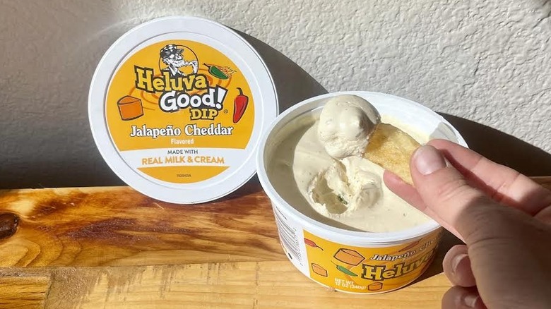 Hand dipping chip into open container of Heluva Good! Jalapeño Cheddar Dip