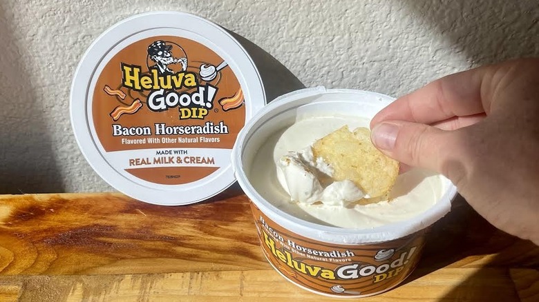 Hand dipping chip into open container of Heluva Good! Bacon Horseradish Dip