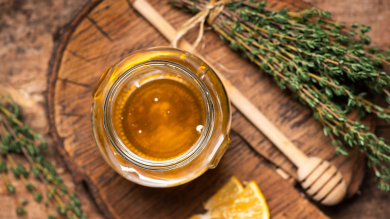 Jar of honey next to rosemary on a wooden board