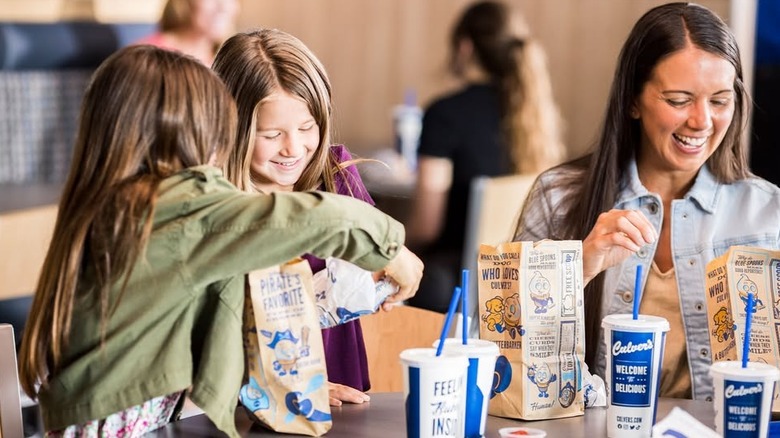 Two kids and an adult at Culver's with kid's meal bags and drinks