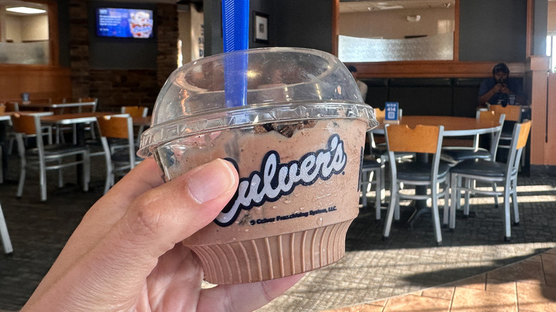 Culver's customer's hand holding chocolate custard cup in dining room with tables in the background