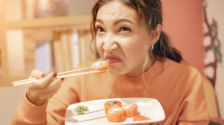 Person grimacing while eating sushi with chopsticks