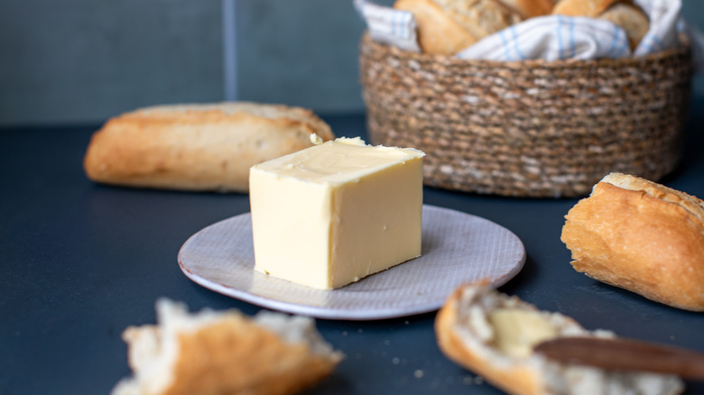 A block of butter is on a plate with loaves of bread arranged around the frame.