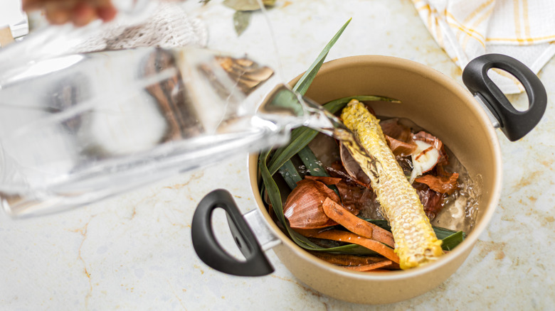 Pouring water into a pot of water and vegetable scraps