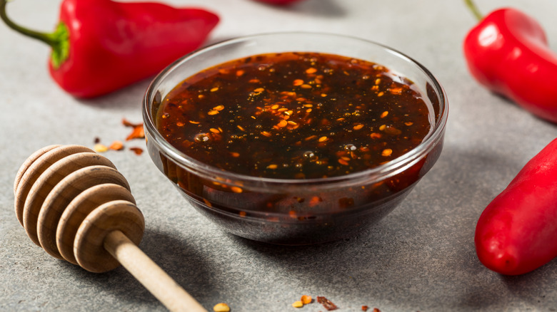 A small glass bowl of honey with chile flakes, surrounded by a honey dipper fresh chiles.