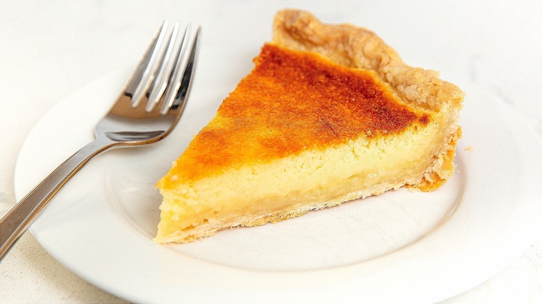 A piece of chess pie on a white plate with a metal fork.