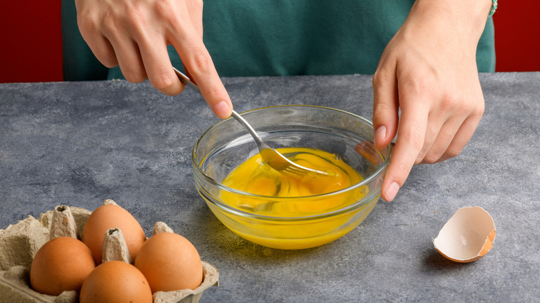A person's hands are seen stirring scrambled eggs with a fork.