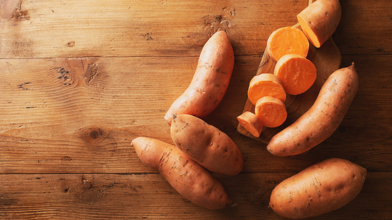 Raw sweet potatoes on wooden cutting board.