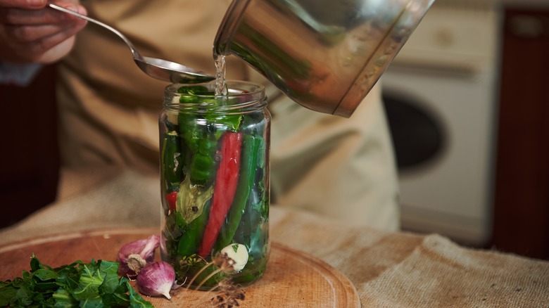 A home cook pours pickling brine from a pan into a jar of peppers.