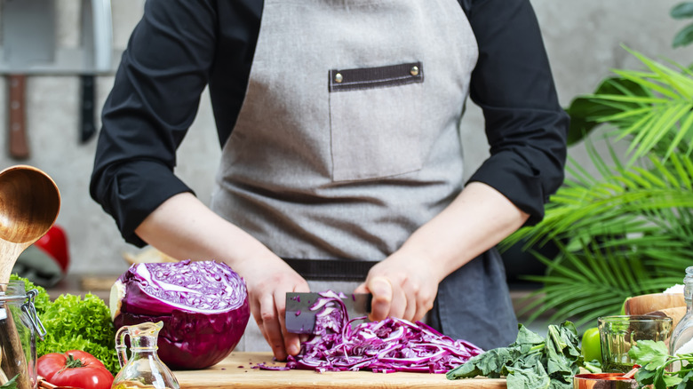 A cook chopping purple cabbage on a cutting board