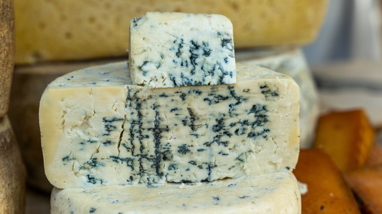 A full blue cheese wheel cut in half, with a smaller chunk atop of it.